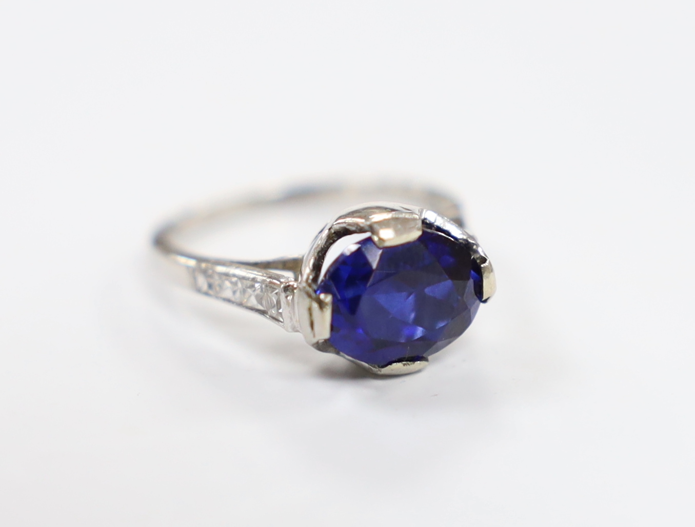 A plat. and iridium, single stone oval cut synthetic sapphire set ring, with graduated diamond chip set shoulders, the shank bearing the signature 'Tiffany & Co', size G, gross weight 3.7 grams.